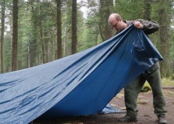 Mann auf Zeltplatz reinigt die Zeltplane (NF)