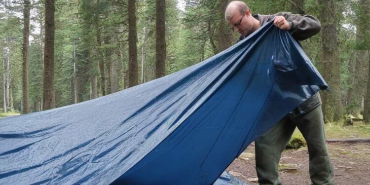 Mann auf Zeltplatz reinigt die Zeltplane (NF)